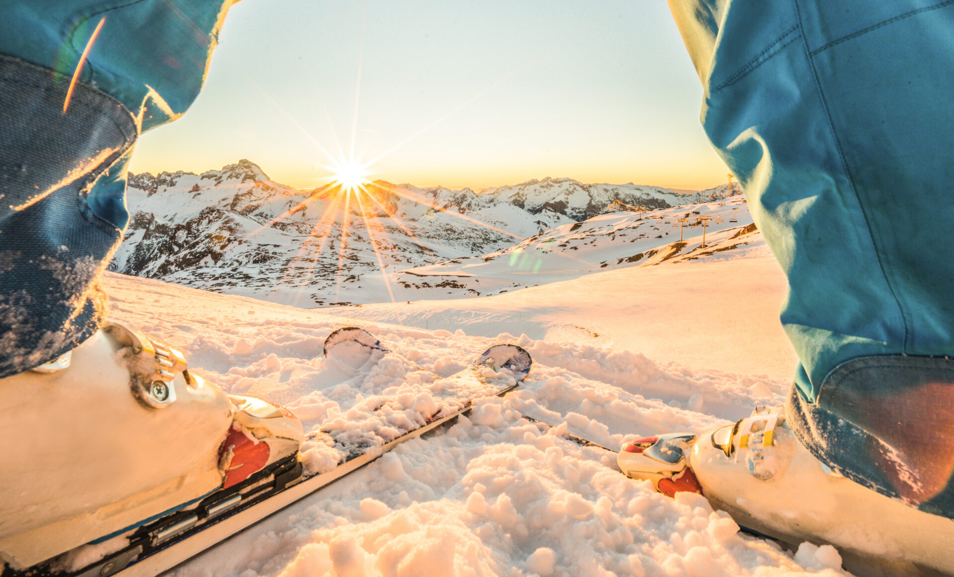 View of a skier's legs and skis, with sunrise over hte mountains in the distance